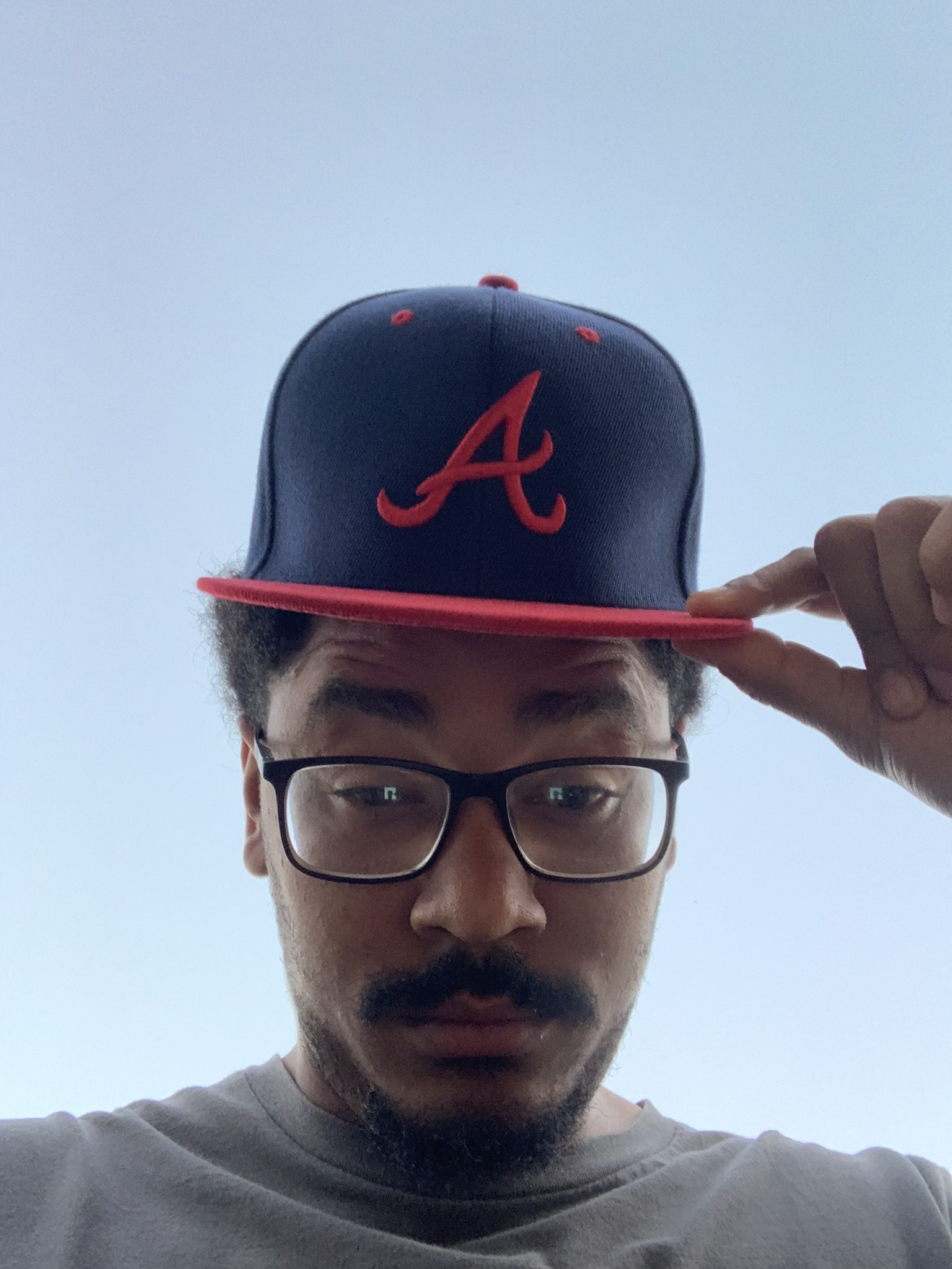 Mr Now wearing glasses and holding the brim of his Atlanta cap